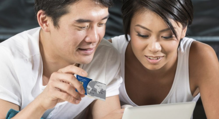 A man and woman looking at a computer screen with a credit card in the man's hand.